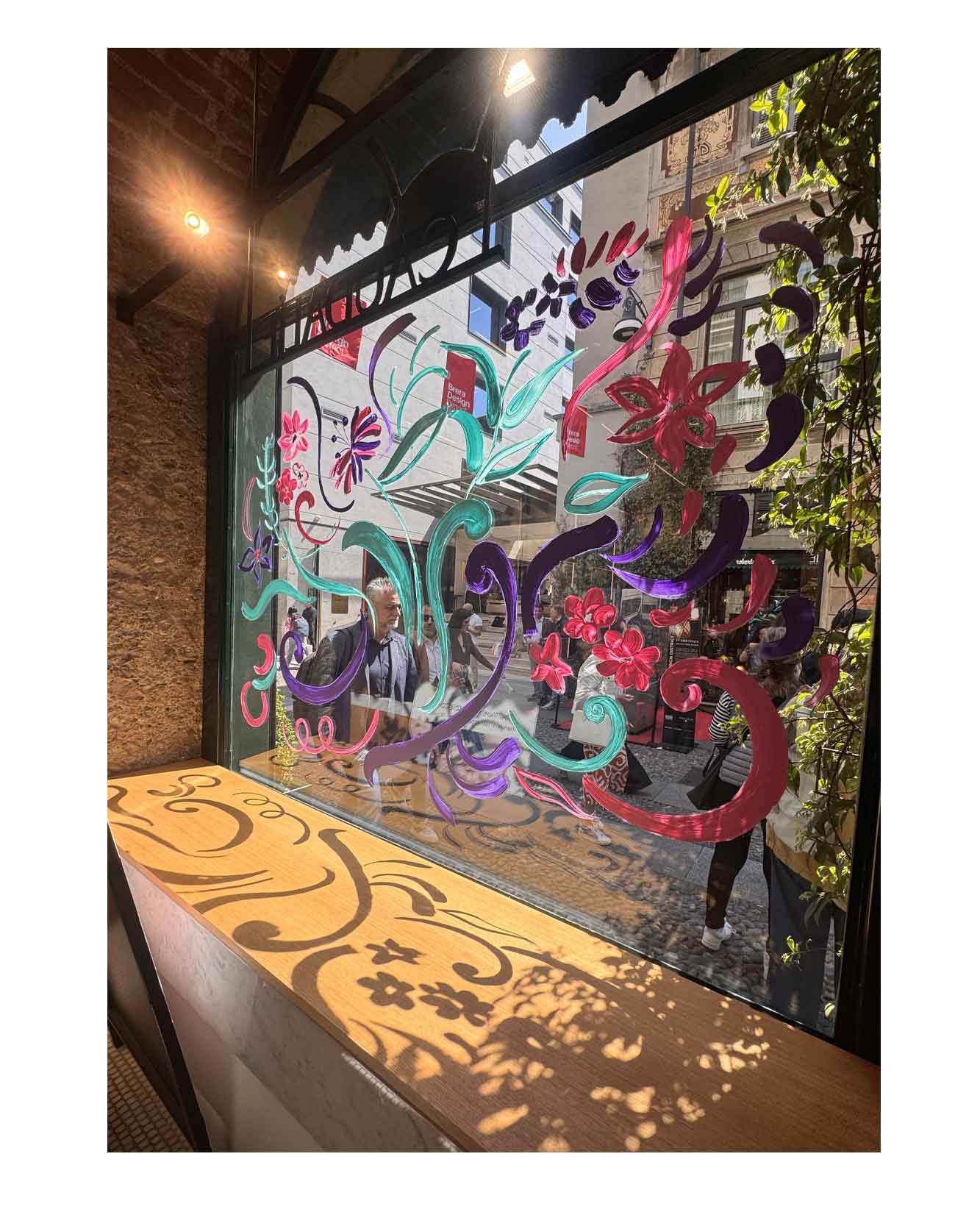 Artist live painting gestural botanical illustrations on large storefront windows during Milan Design Week for a luxury beauty brand, featuring fluid ink lines inspired by nature and fragrance.