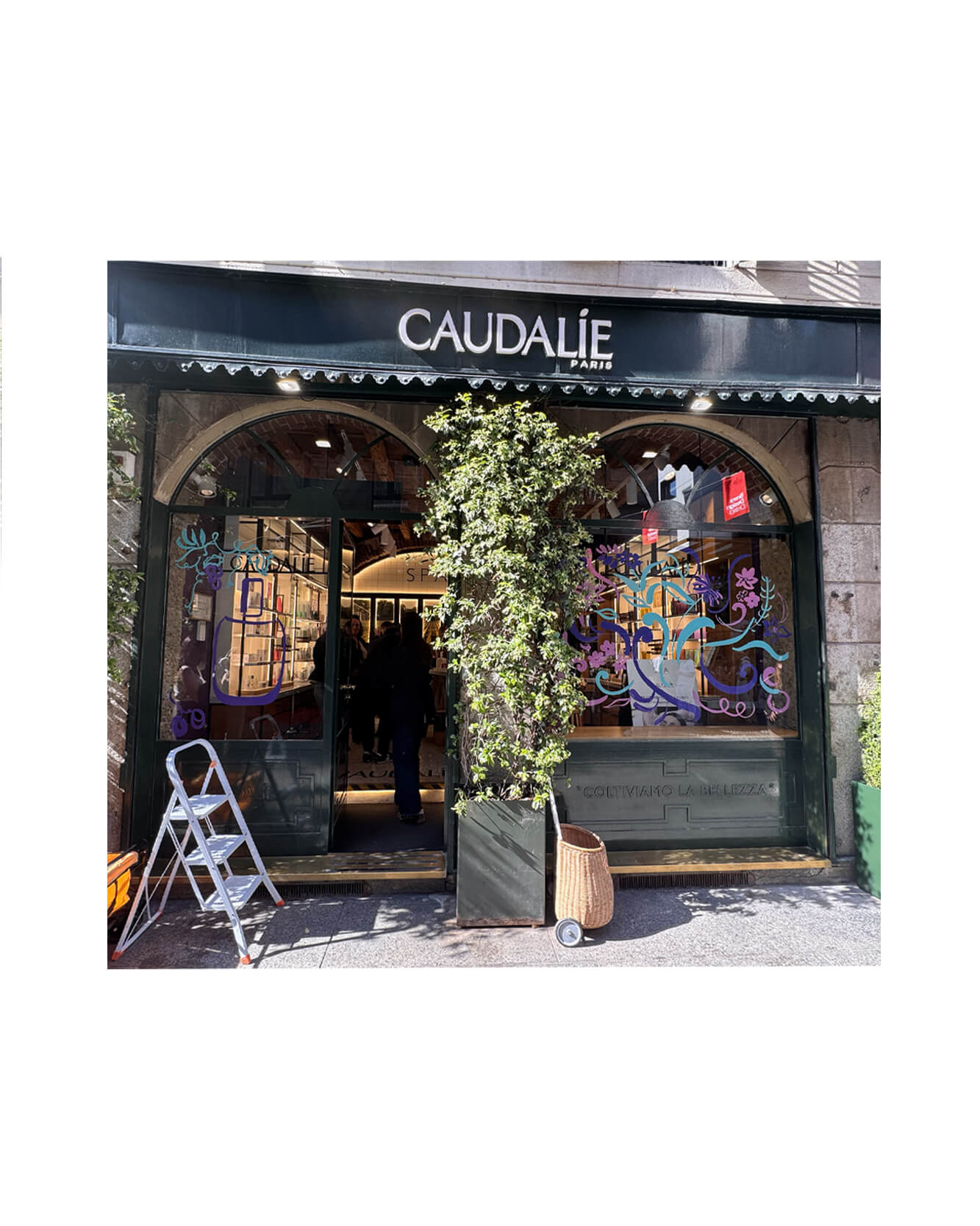Artist live painting gestural botanical illustrations on large storefront windows during Milan Design Week for a luxury beauty brand, featuring fluid ink lines inspired by nature and fragrance.