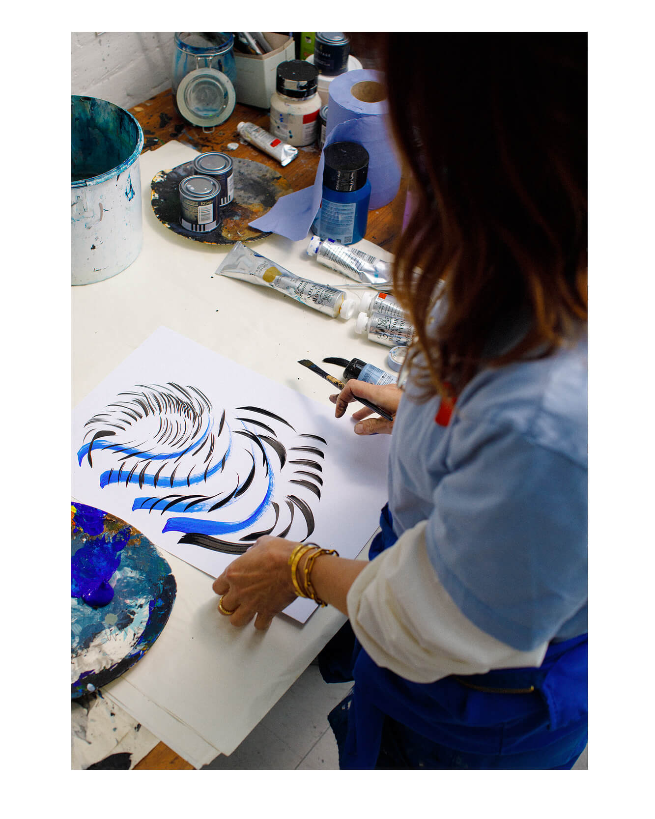 Photograph taken from above of illustrator and artist Caroline Tomlinson creating gestural marks in blue and black ink and paint.