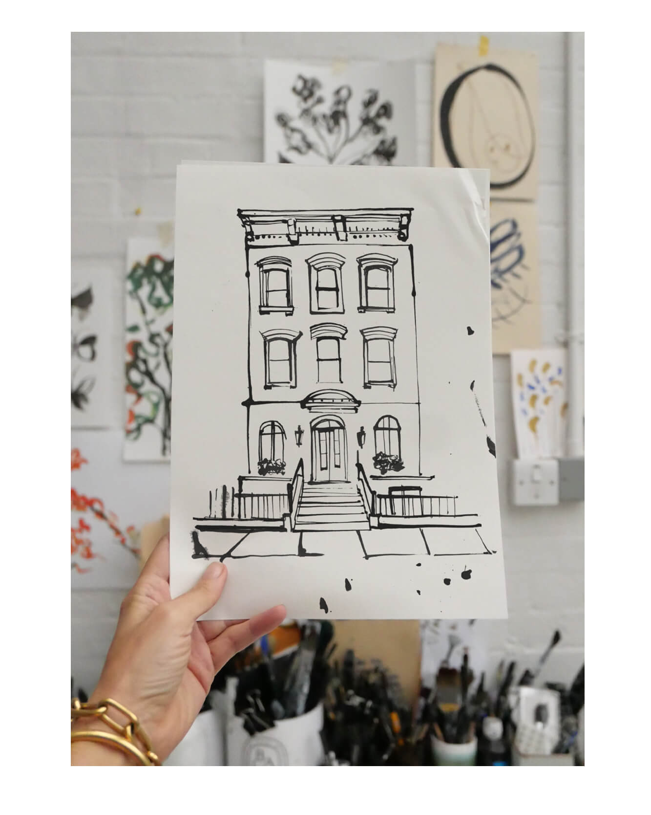 and-drawn ink illustration of a New York brownstone townhouse, held up against a studio wall covered in sketches.